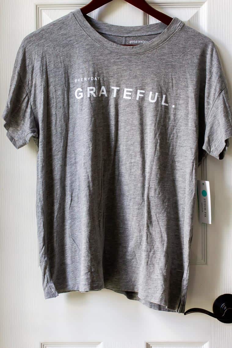 A gray tee shirt on a hanger in front of a white door