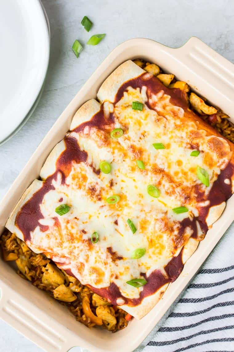 Blue Apron's Chicken Enchiladas in a baking dish with a black and white stripe napkin, plates, and green onions on a white background
