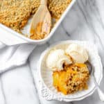 overhead view of peach crisp in a bowl with ice cream and part of the baking dish showing