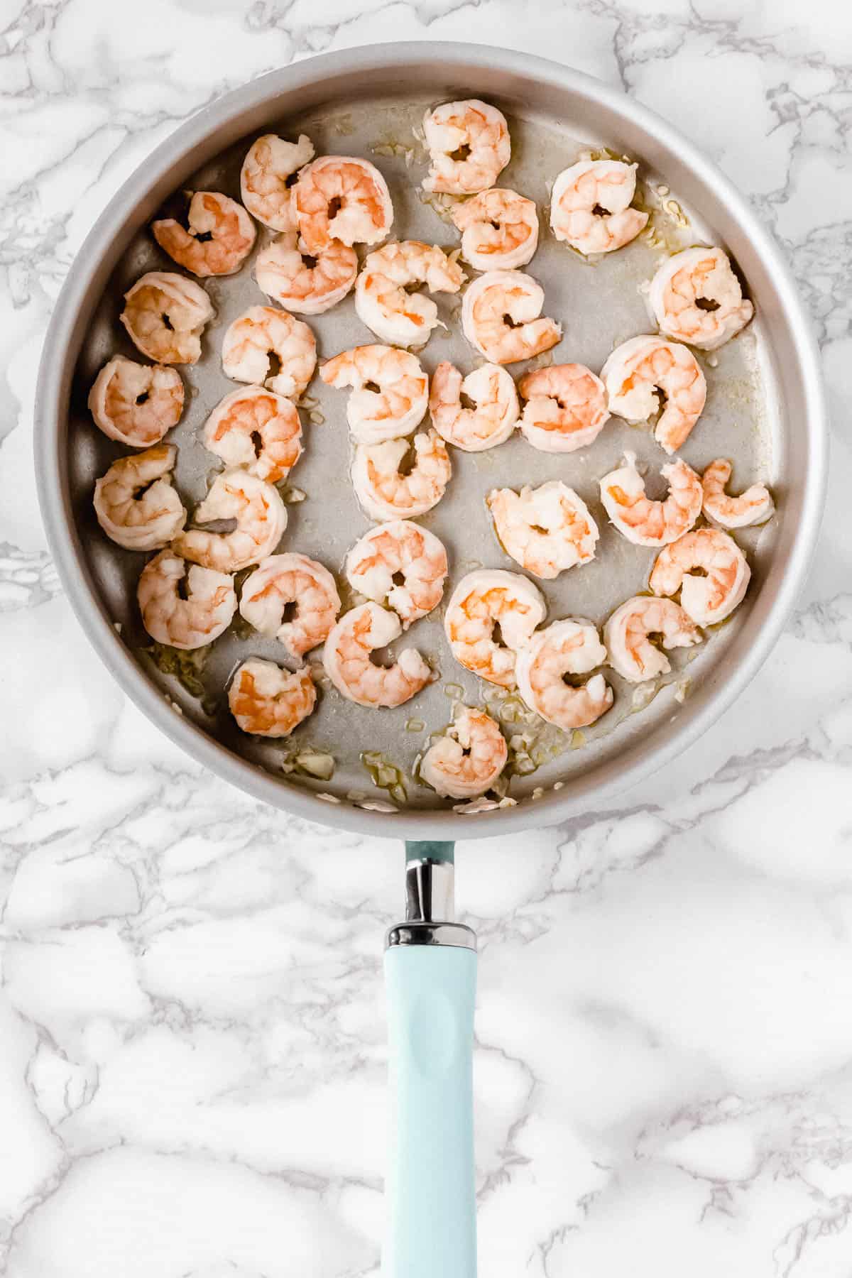 Shrimp cooking in a silver skillet over a marble background
