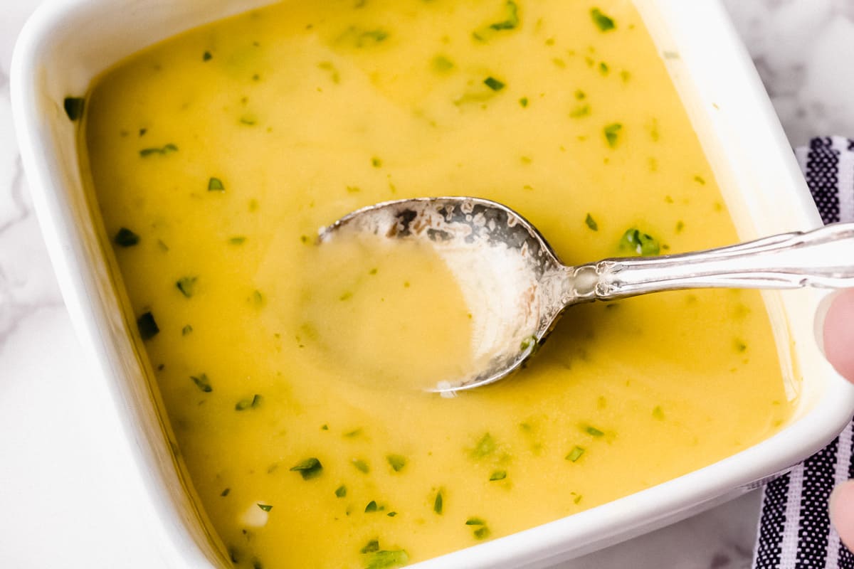 Honey lime dressing in a square white bowl with a silver spoon lifting some up