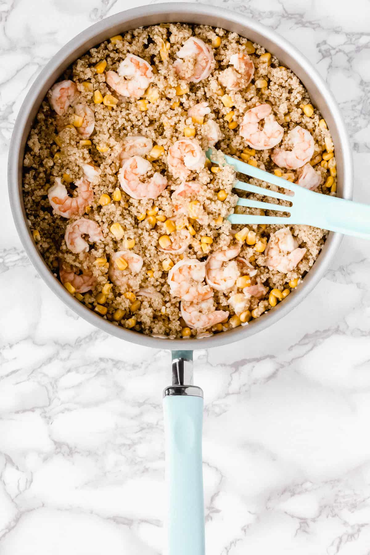 Shrimp and quinoa salad in a skillet with a teal turner in it over a marble background