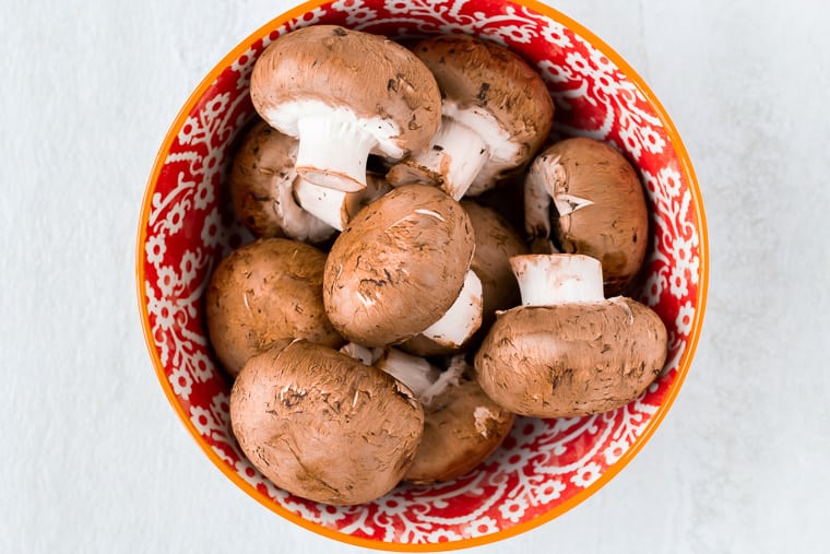 Whole mushrooms in a red bowl on a white background