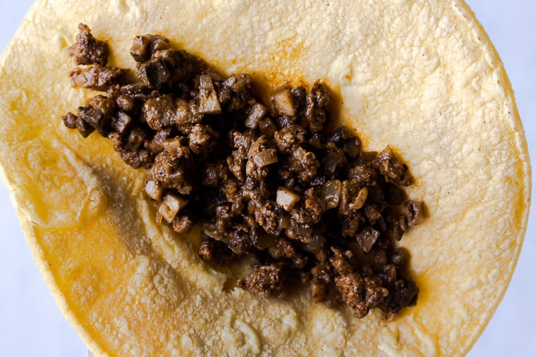 A corn tortilla filled with ground beef and mushrooms on a white background