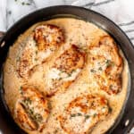 Overhead view of chicken with creamy dijon mustard sauce in a black skillet over a marble background with fresh thyme, a head of garlic and a striped towel around it with text overlay.