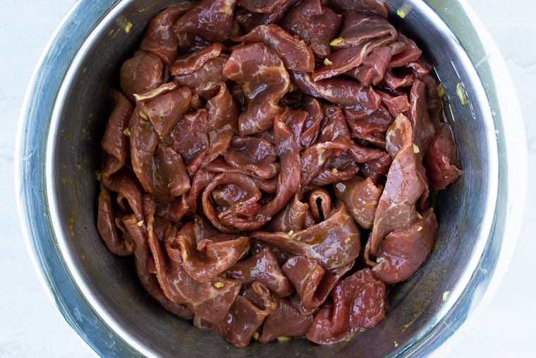 Beef strips marinating in a silver bowl