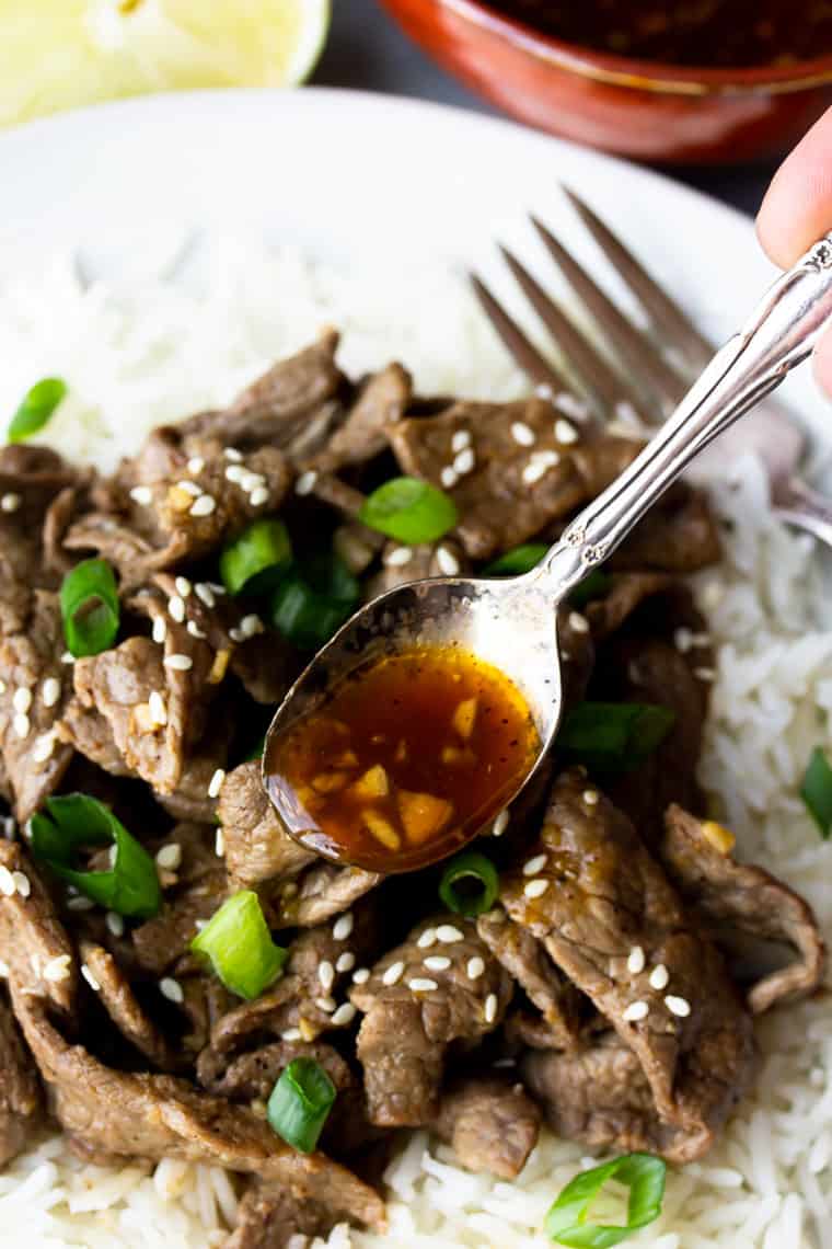 Ginger Beef over white rice on a white plate with extra sauce being spooned over it 