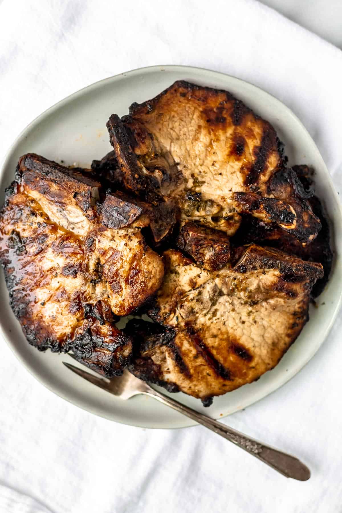 Overhead of grilled Cuban pork chops on a white plate with a fork.