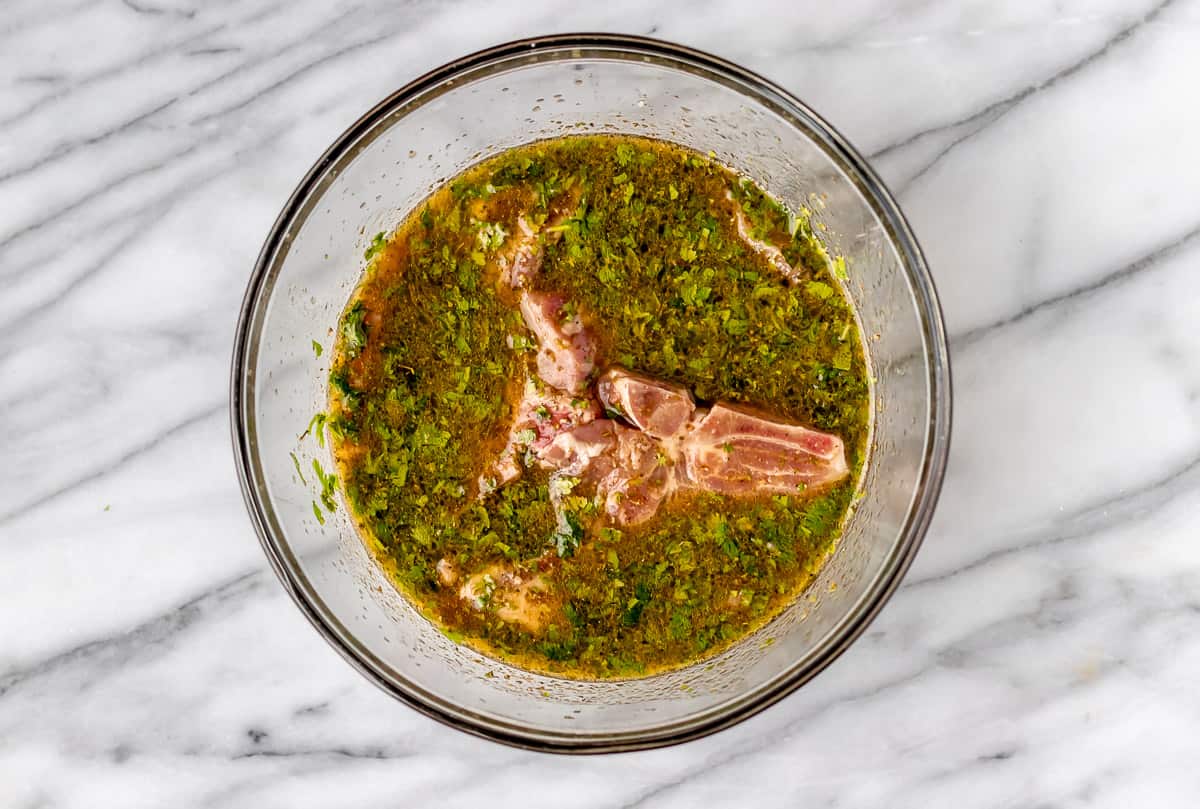 Pork chops in a glass bowl of cuban marinade.