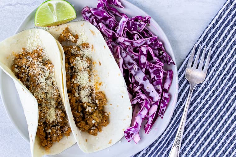 Blue Apron Tomatillo Pork Tacos on a white plate with a blue and white stripe napkin and fork over a white background