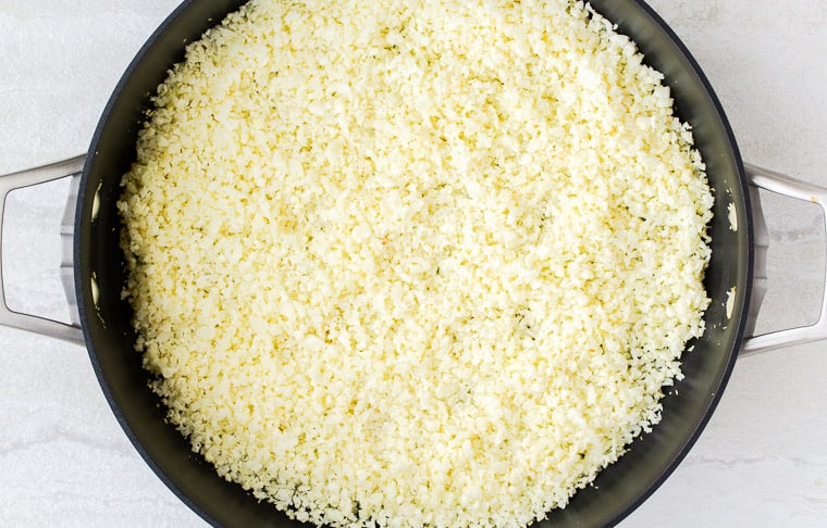 cauliflower rice in a black skillet over a white background