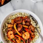 Overhead of a white bowl filled with cauliflower rice and jambalaya with the black skillet in the background with text overlay.