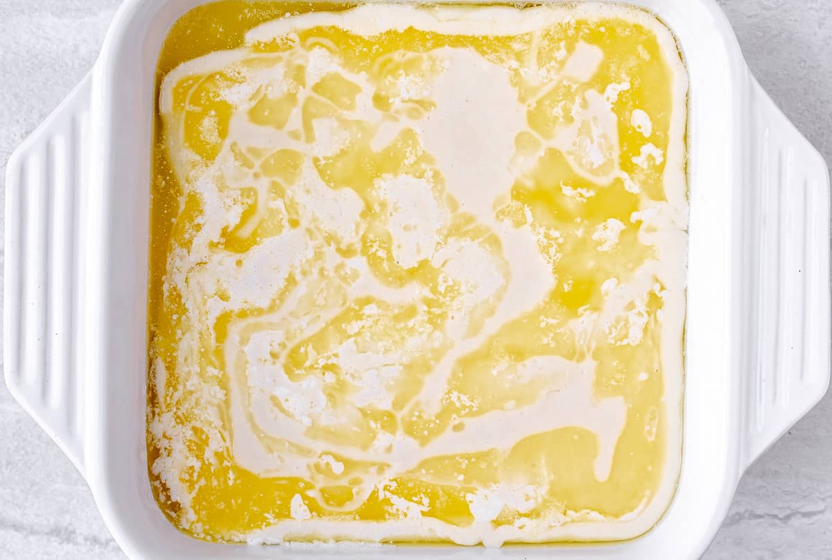 Melted butter and cobbler batter in a white, square baking dish