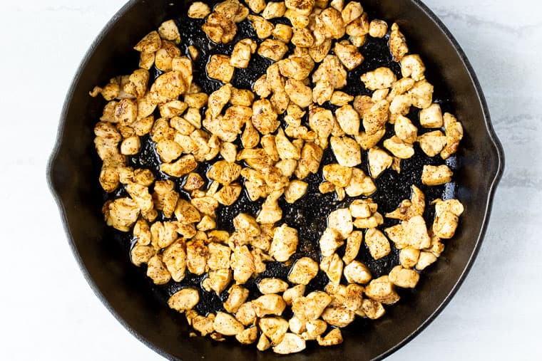 Chicken cubes cooking in a black cast iron skillet over a white background