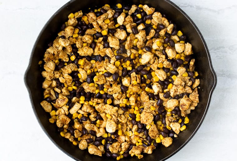 Chicken, corn, and black beans in a cast iron skillet over a white background