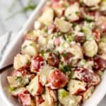 Tarragon potato salad in a shallow, oval serving dish with a spoon in it with text overlay.