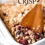 Blackberry crisp being lifted up on a wood server with text overlay.