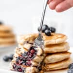 A stack of blueberry pancakes on a fork with text overlay.