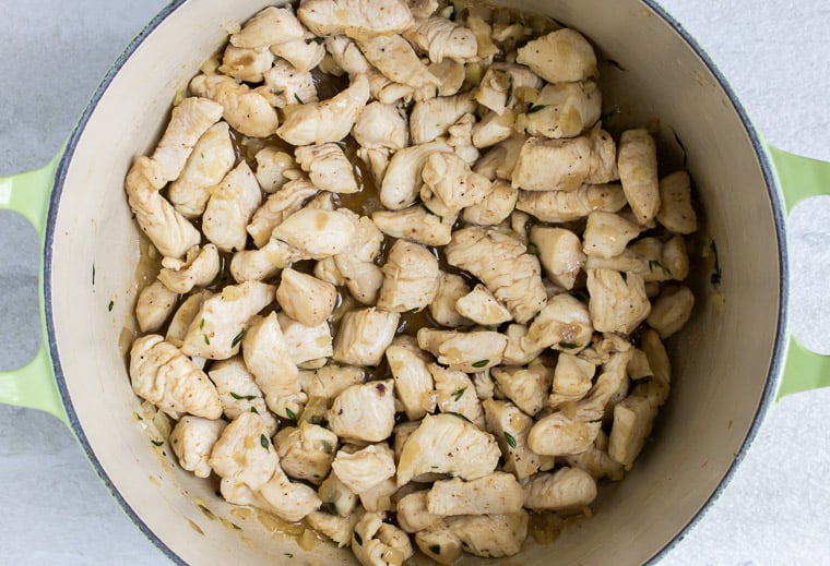 Pieces of chicken cooking in a Dutch oven over a white background