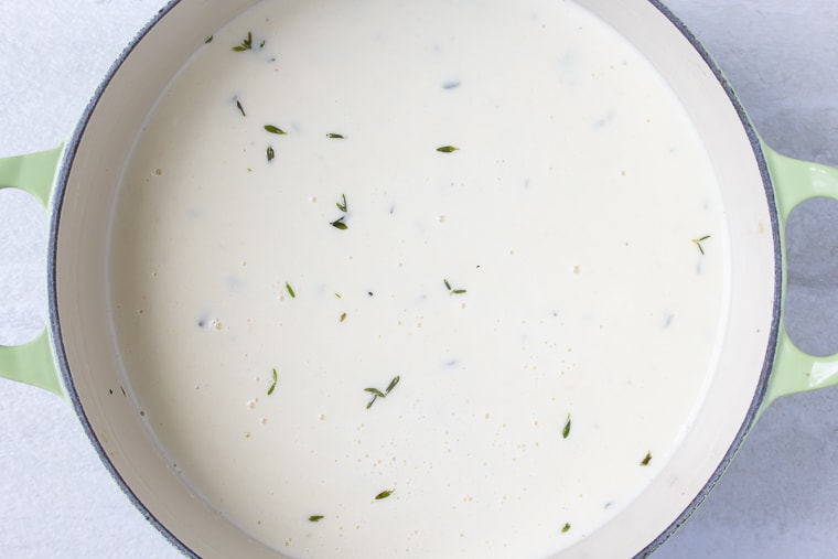 Cream sauce cooking in a Dutch oven over a white background