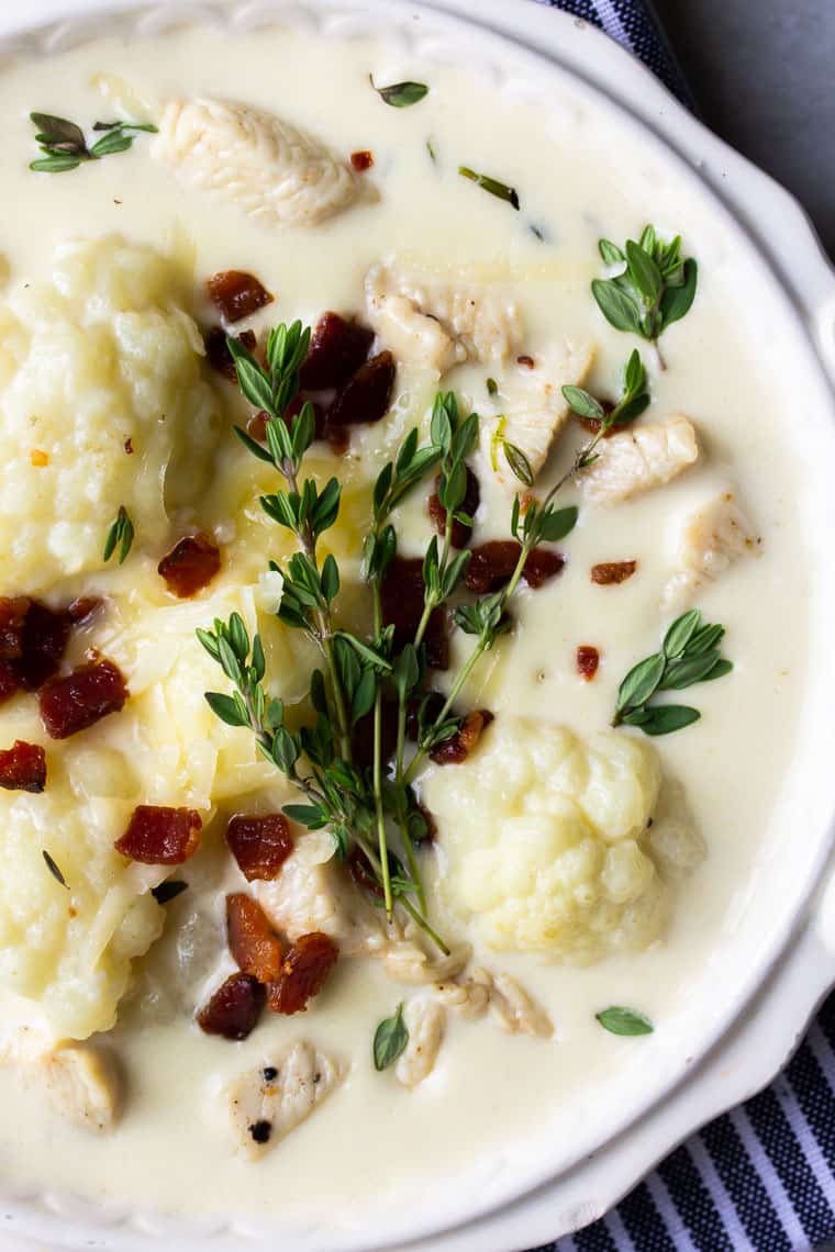 Close up of a bowl of Cauliflower Chicken Chowder in a white bowl with a blue and white napkin