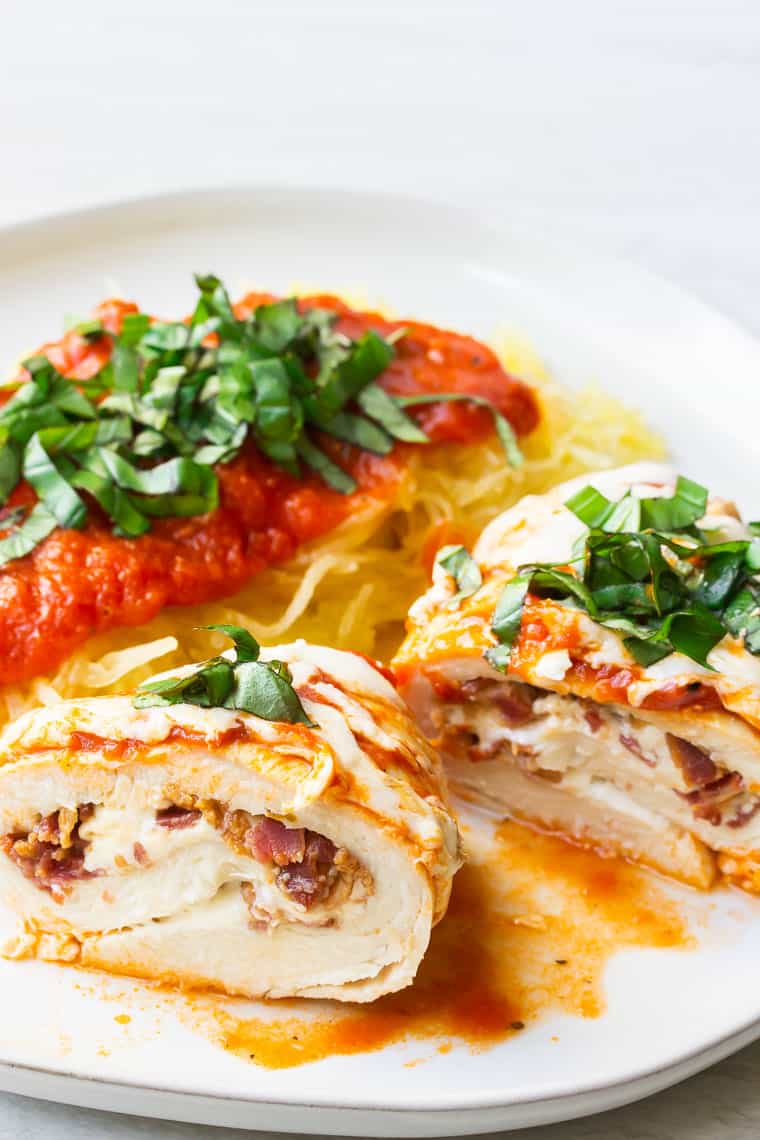 A chicken roll up cut in half on a white plate with spaghetti squash and fresh basil