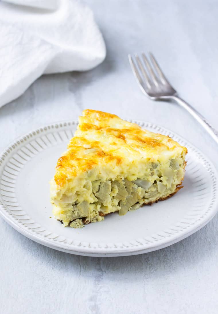 A slice of Artichoke and Shallot Frittata on a white plate with a fork and white napkin in the background