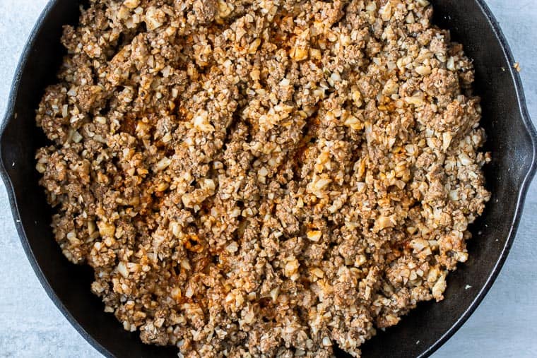 Ground beef and cauliflower rice cooking in a black skillet