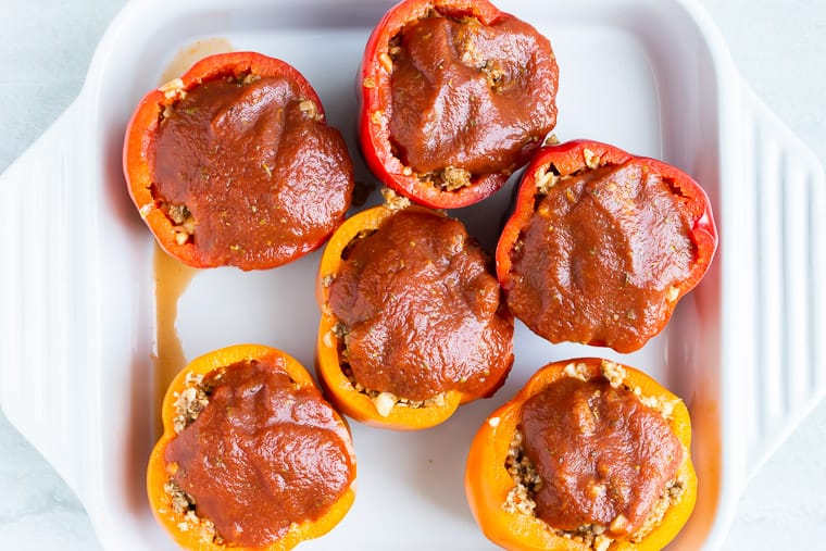 6 Peppers stuffed with beef and topped with tomato sauce in a white casserole dish