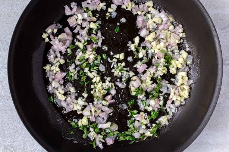 Shallot, garlic, and thyme cooking in a black skillet
