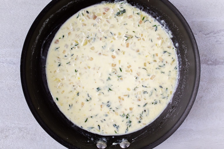 Cream sauce cooking in a black skillet over a white background