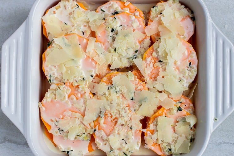 Butternut squash rounds topped with a cream sauce and Parmesan cheese in a white, square baking dish