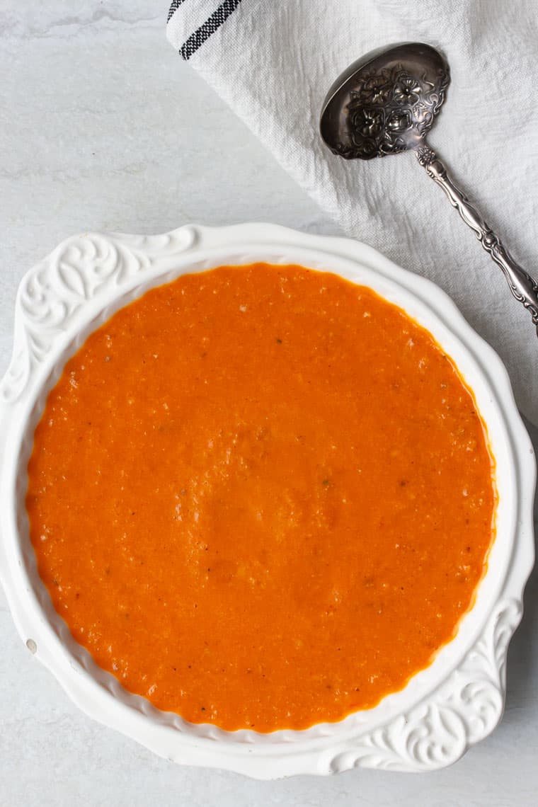 Romesco sauce in a white bowl with a white napkin and metal spoon next to it over a white background