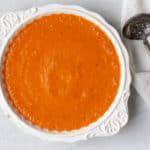 Romesco Sauce in a white bowl over a white background with a metal spoon and black and white towel