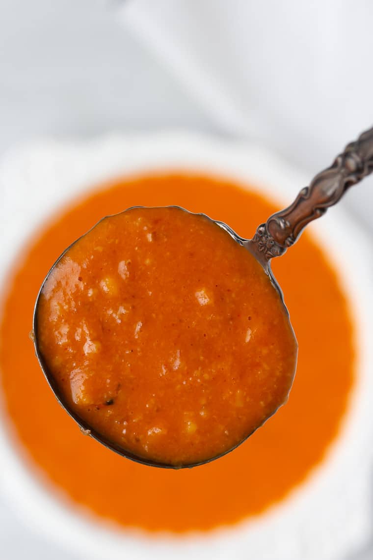 A spoonful of romesco sauce being lifted out of a white bowl over a white background