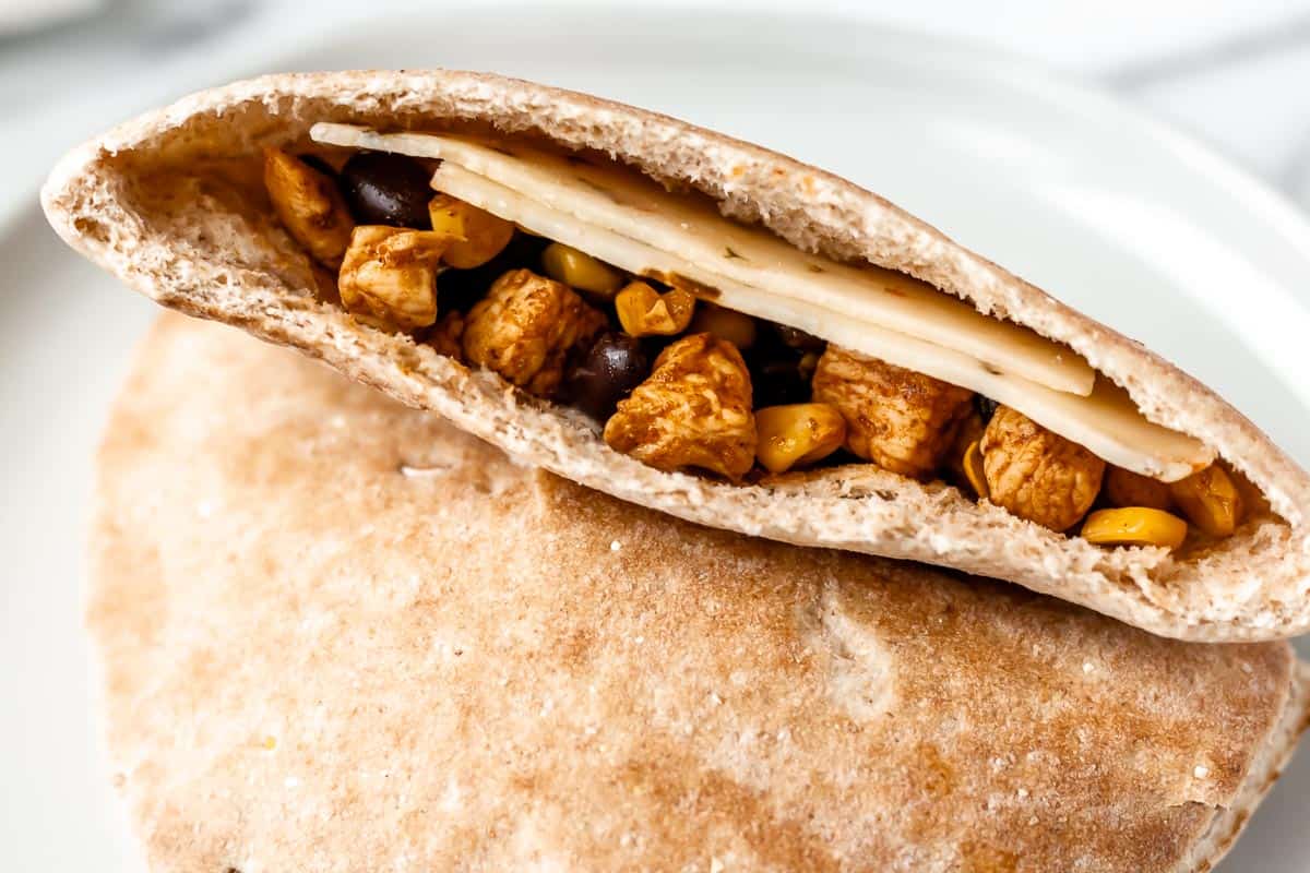 A pita pocket with chicken, corn and black beans inside.