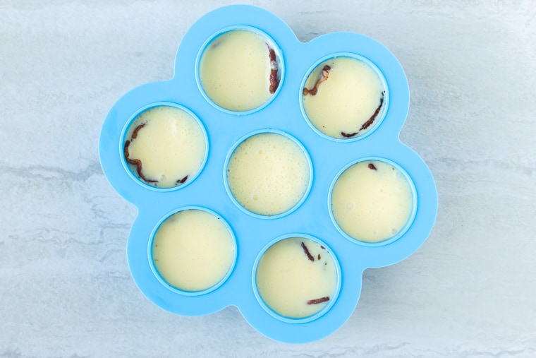 A blue egg bites mold filled with egg mixture over a white backdrop