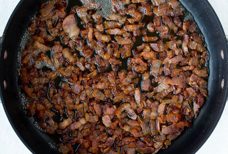 Diced bacon cooking in a black skillet