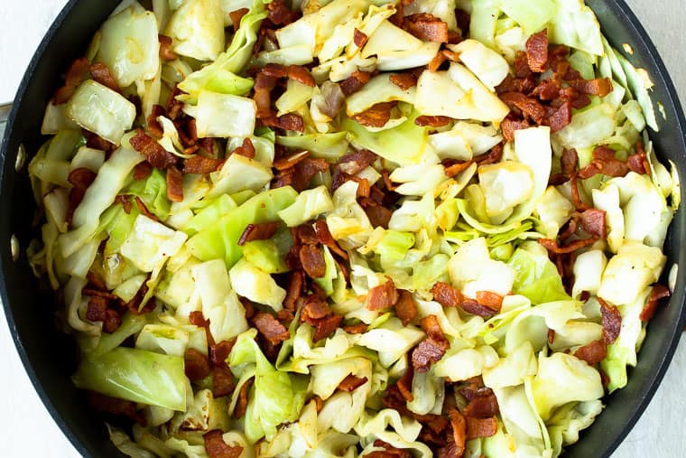 Fried cabbage and bacon in a black skillet