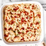 Keto au gratin cauliflower topped with bacon in a square, white casserole dish.