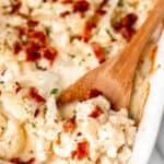 Close up of keto cauliflower au gratin topped with bacon with a spoon in it with text overlay.