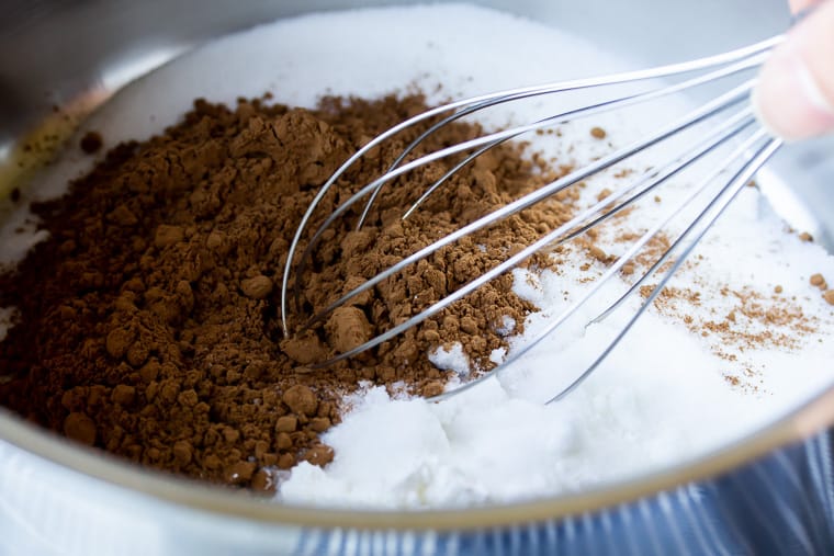 Close up of a silver saucepan with cocoa powder, sugar, and a whisk in it