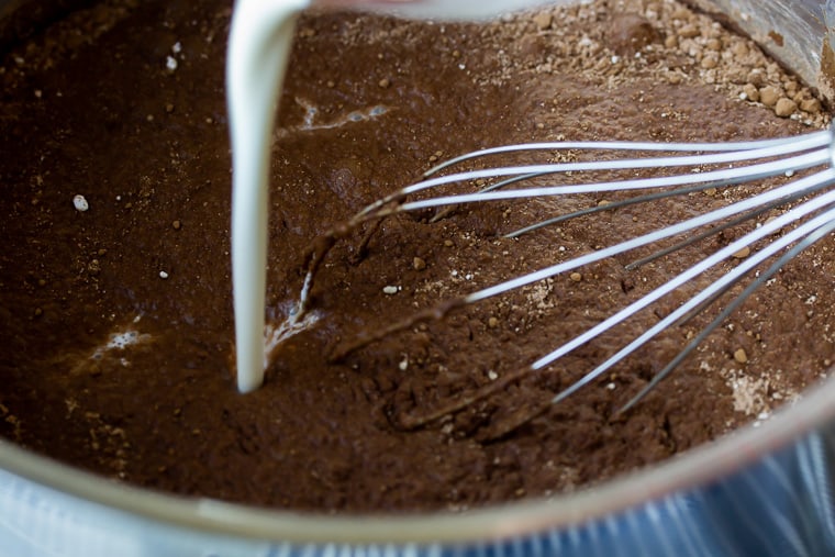 Cream being poured into a chocolate mixture in a sauce pan with a whisk