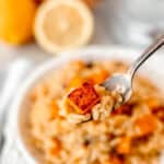 A forkful of lemon risotto with a cube of roasted butternut squash on it being held up in front of the bowl with text overlay.