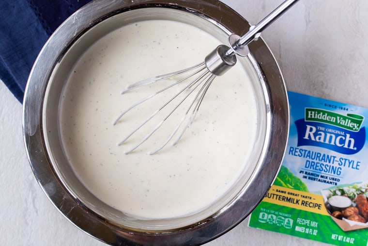 Homemade Ranch Dressing in a silver bowl with a whisk in it and a blue napkin and ranch seasoning packet next to it