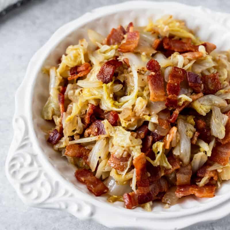 Close-up of a white bowl filled with fried cabbage and crispy bacon pieces, showing tender cabbage mixed with browned bacon in a savory skillet-style dish.