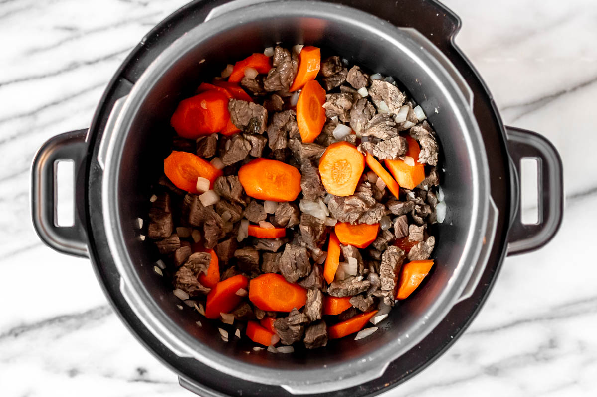 Beef, carrots, onion and garlic cooking in the bottom of an Instant Pot.