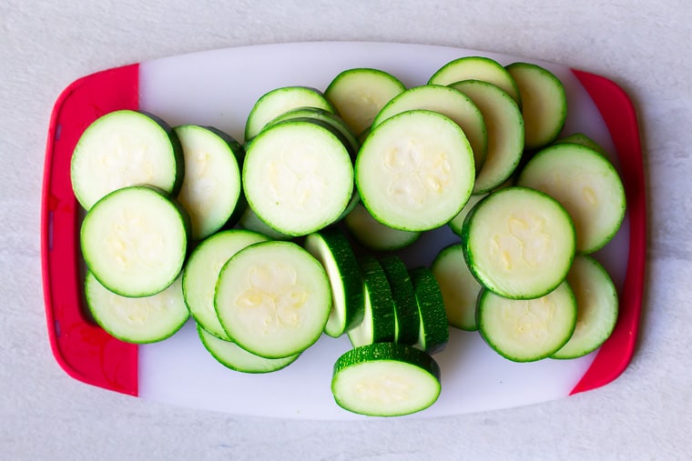Zucchini cut into rounds on a red and white cutting board