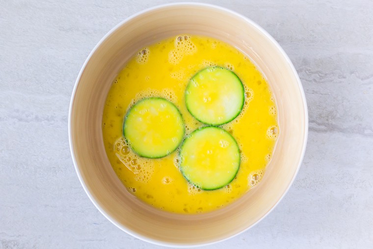 3 Zucchini Rounds in an egg wash in a white bowl