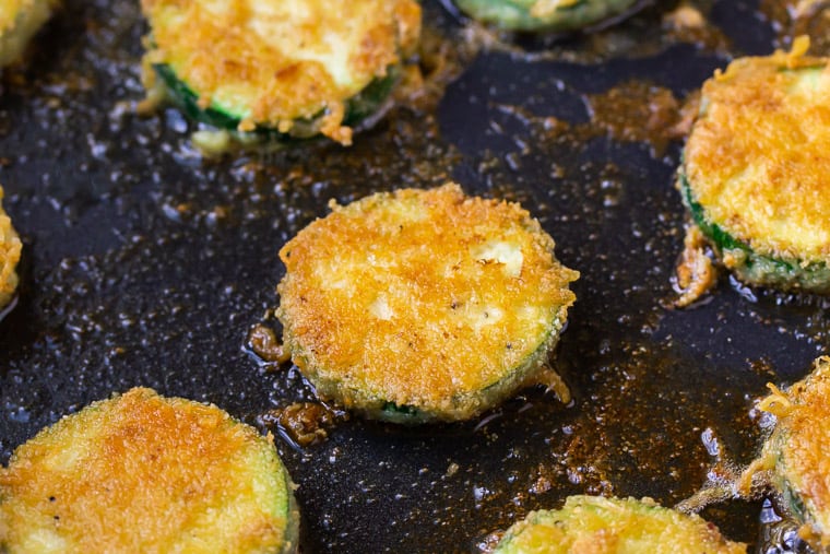 Close up of a slice of zucchini frying in a black skillet